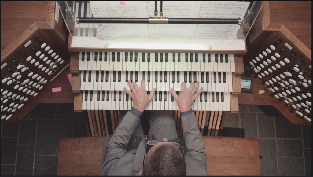 Photo looking down on Christopher playing the 3 keyboards of an organ